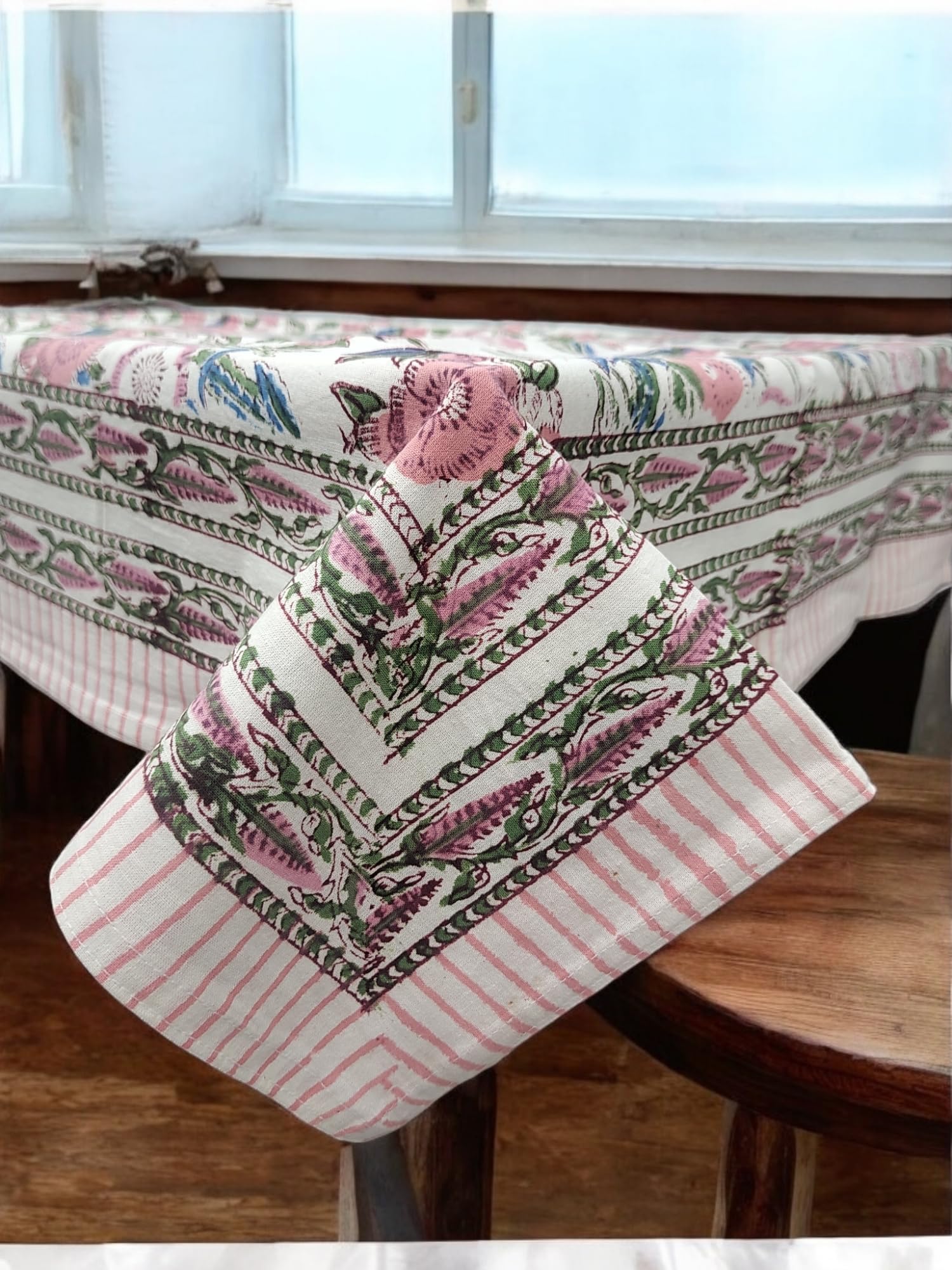 Elegant white and pink floral hand block print tablecloth draping over a wooden table, adding charm to dining decor.