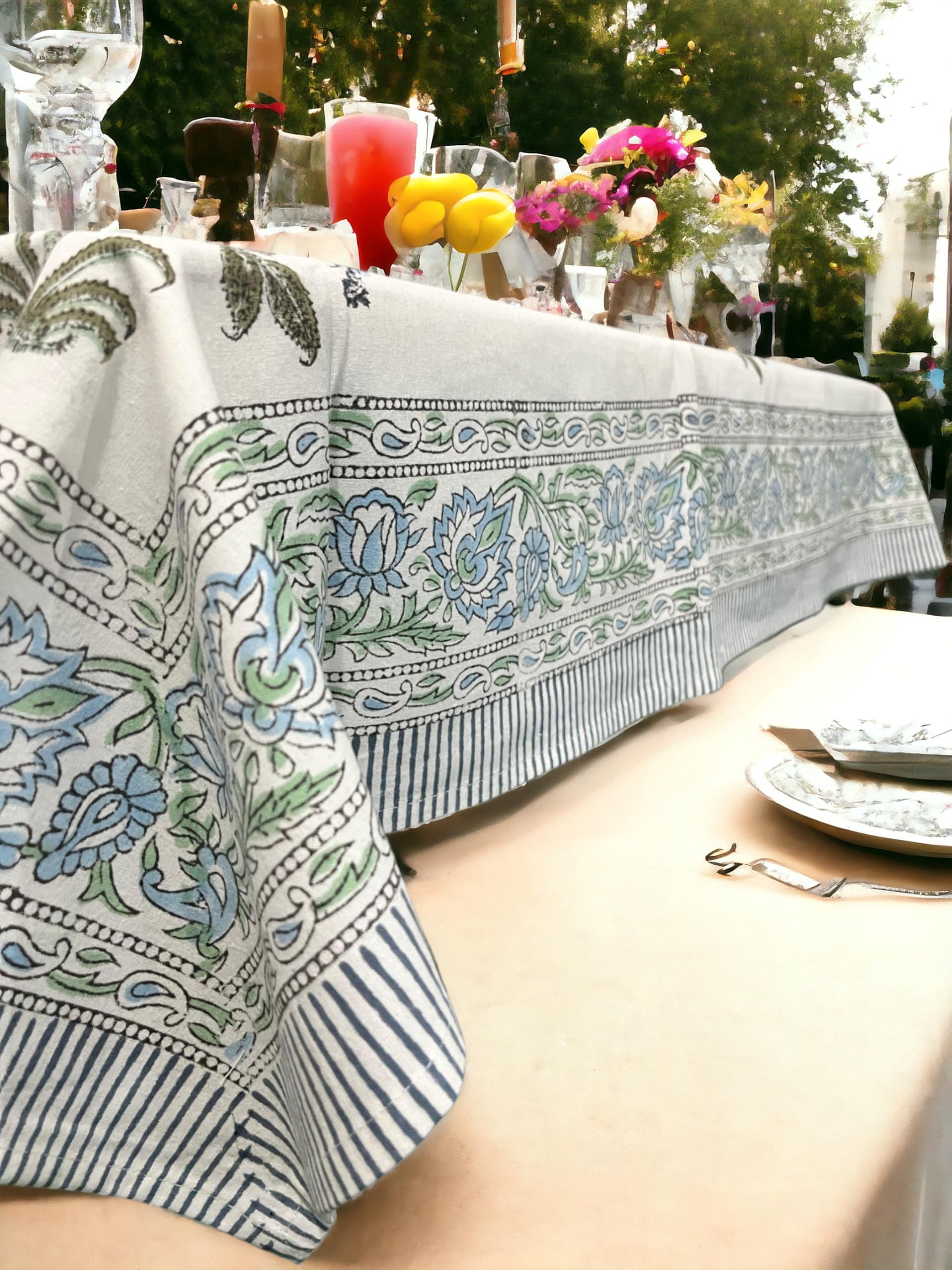 Colorful bohemian floral hand block print tablecloth draping over outdoor dining table with plates and drinks.
