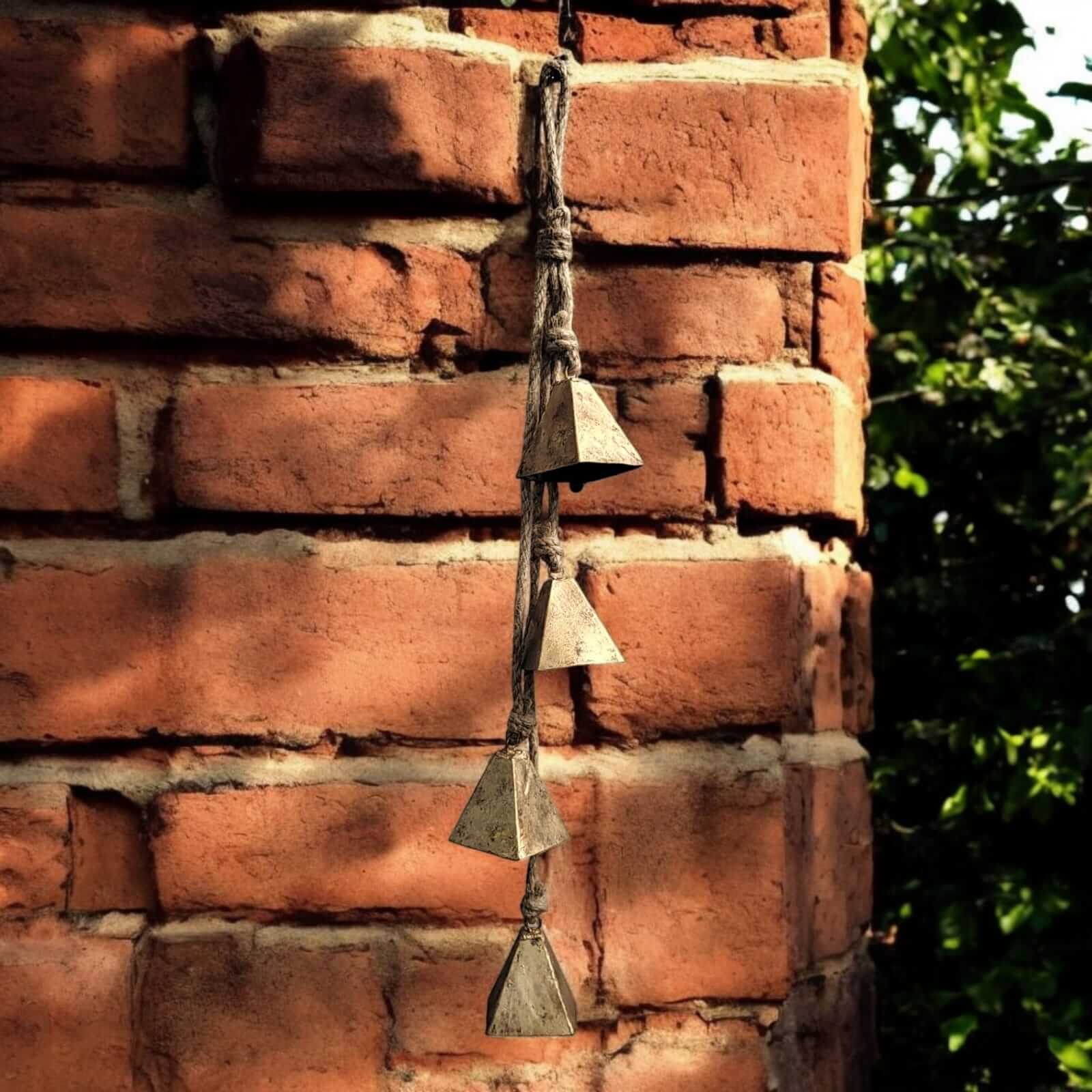 Rustic iron wind chime with triangle bells hanging from a brick wall, creating a tranquil outdoor ambiance.