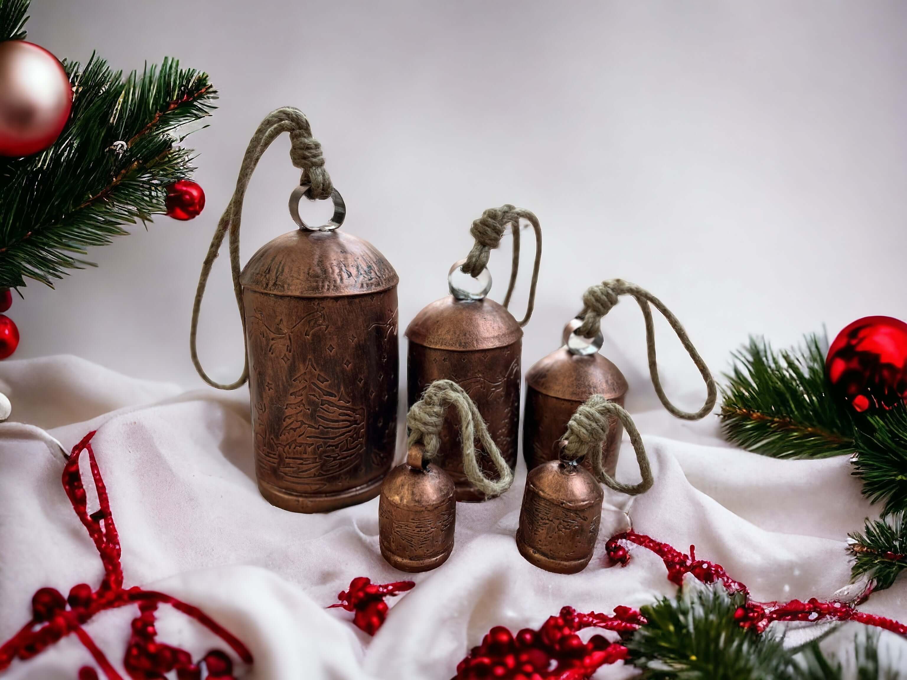 Set of 5 rustic giant cow bells with jute handles for Christmas decoration, surrounded by greenery and festive ornaments.