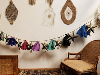 Handmade upcycled silk sari garland with metal stars and bells, colorful bohemian decoration in cozy interior setting.