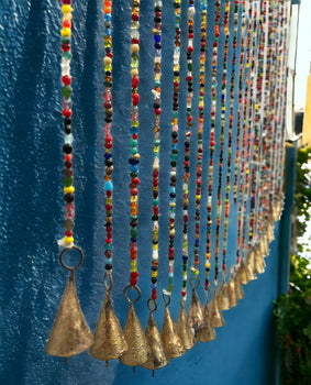 Colorful bohemian glass beaded curtain with gold bells hanging against a blue wall.