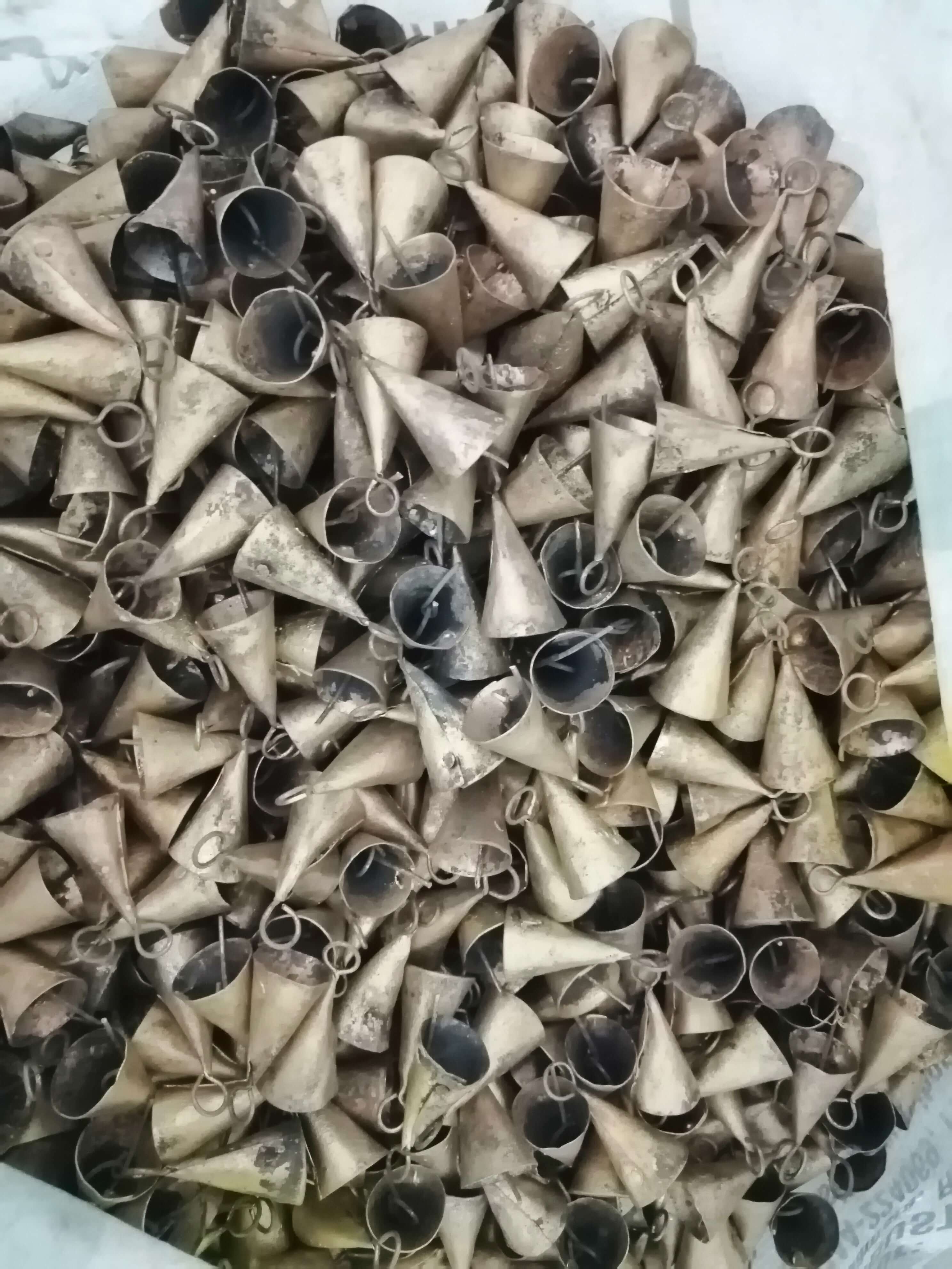 A pile of rustic cone-shaped bells made from recycled iron, showcasing various shades and a handmade finish.