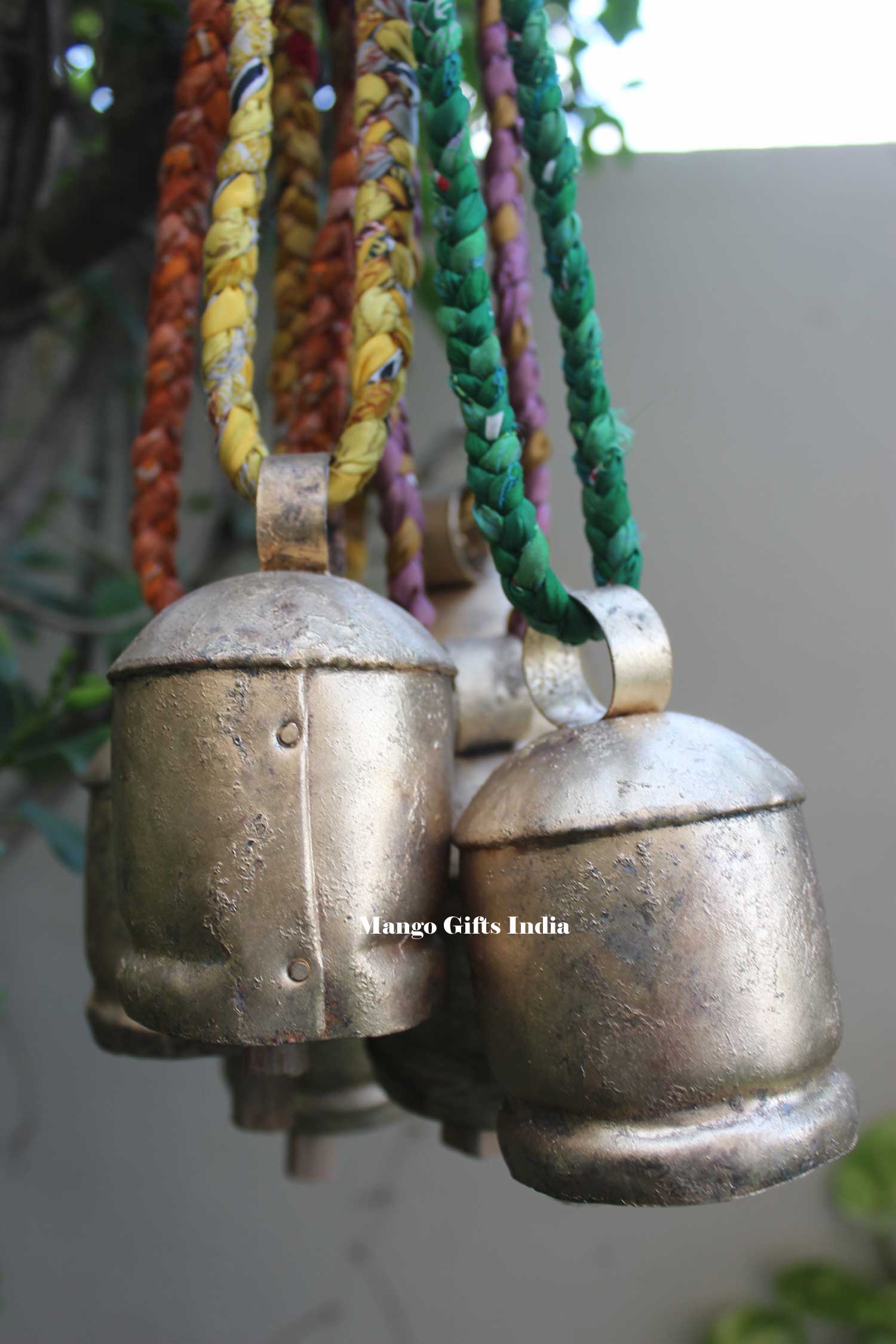 Set of 6 rustic antique tin cow bells with colorful braided sari fabric handles for garden decor.