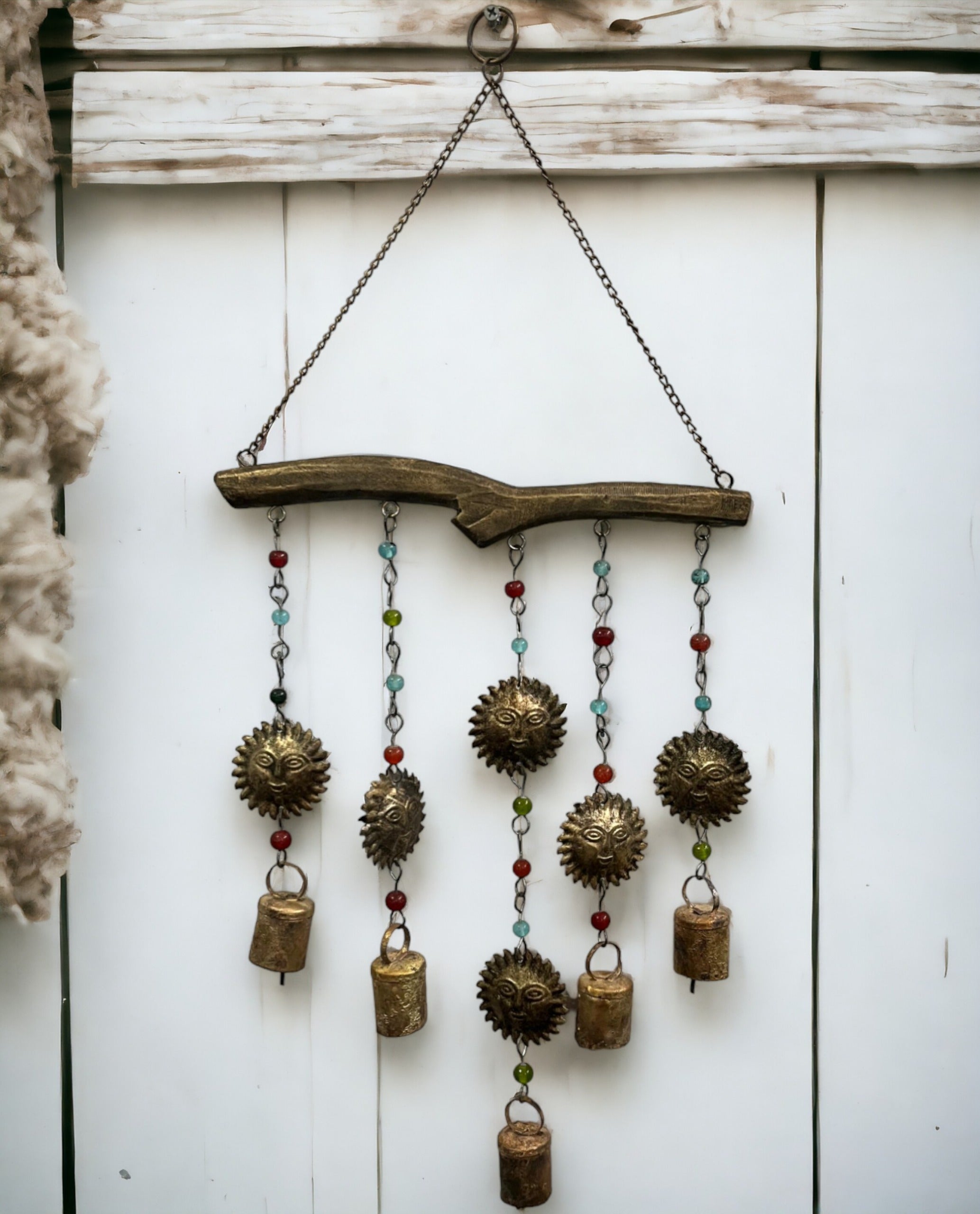 Handmade boho wind chime with decorative bells and glass beads, featuring sun and star designs, hanging from a branch.