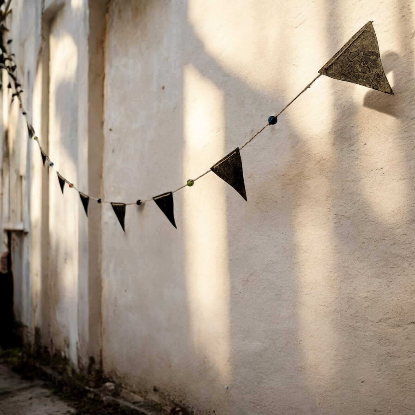 Recycled iron triangle bunting garland with multicolored glass beads hanging on a wall, perfect for bohemian decor.