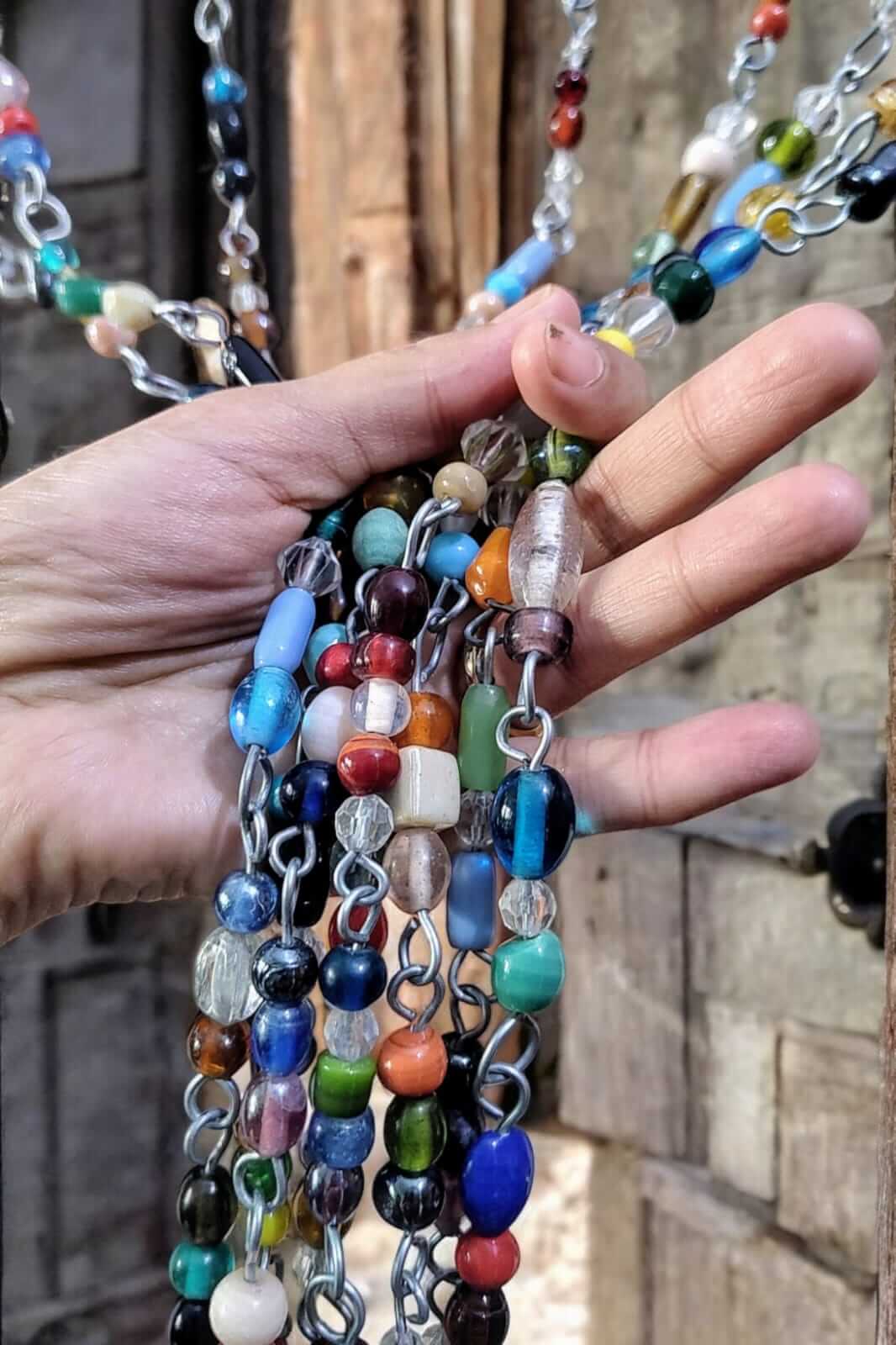Hand holding vibrant strands of glass beads and metal chains for bohemian beaded curtains and sun catchers.