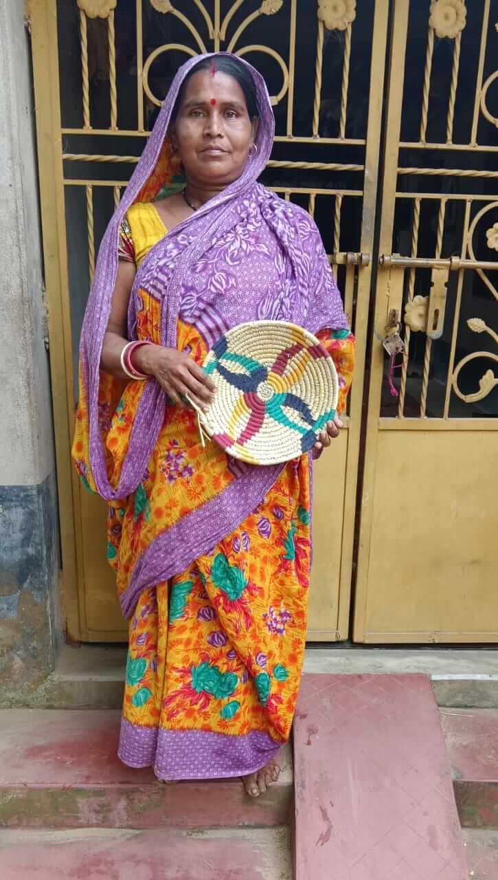 Woman in colorful traditional attire holding a handcrafted woven basket near a decorative door.