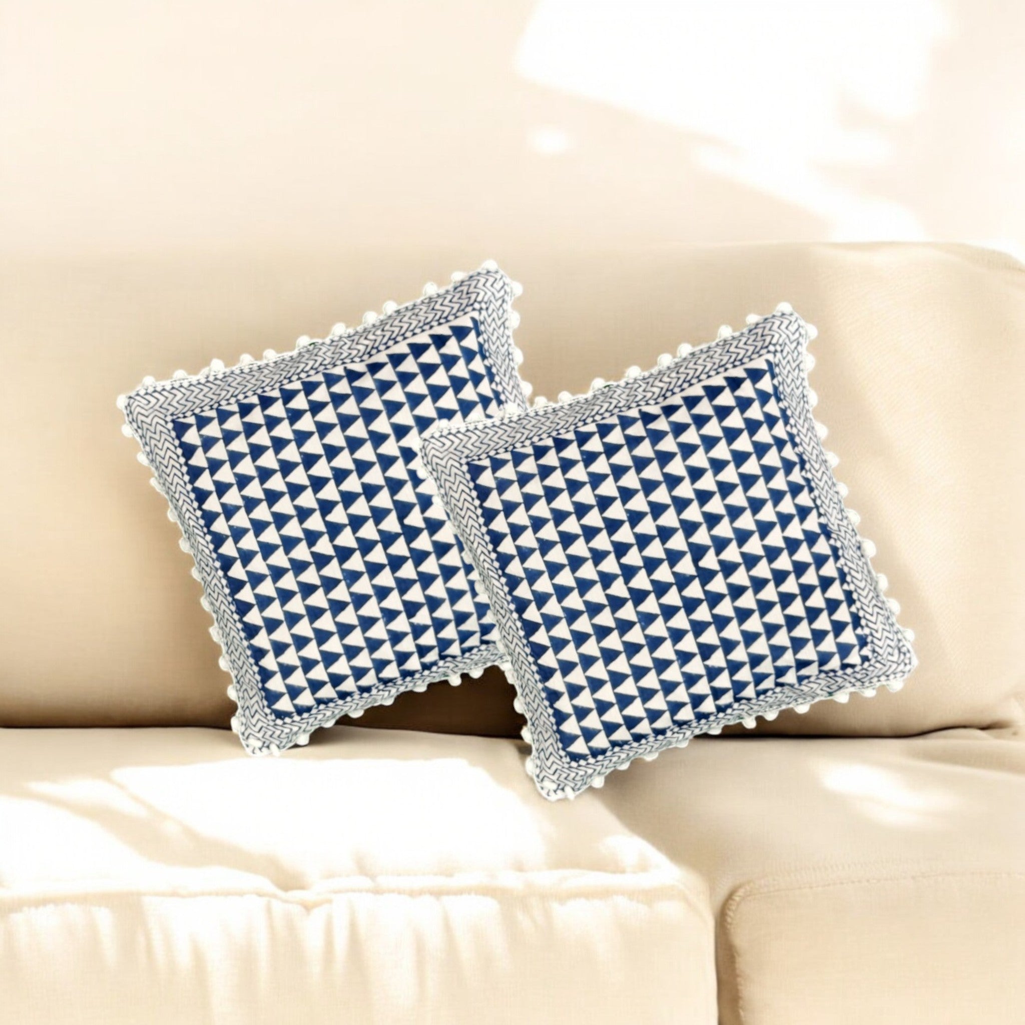 Set of 2 blue and white geometric triangle pattern cushion covers with pom-pom fringe on a sofa.
