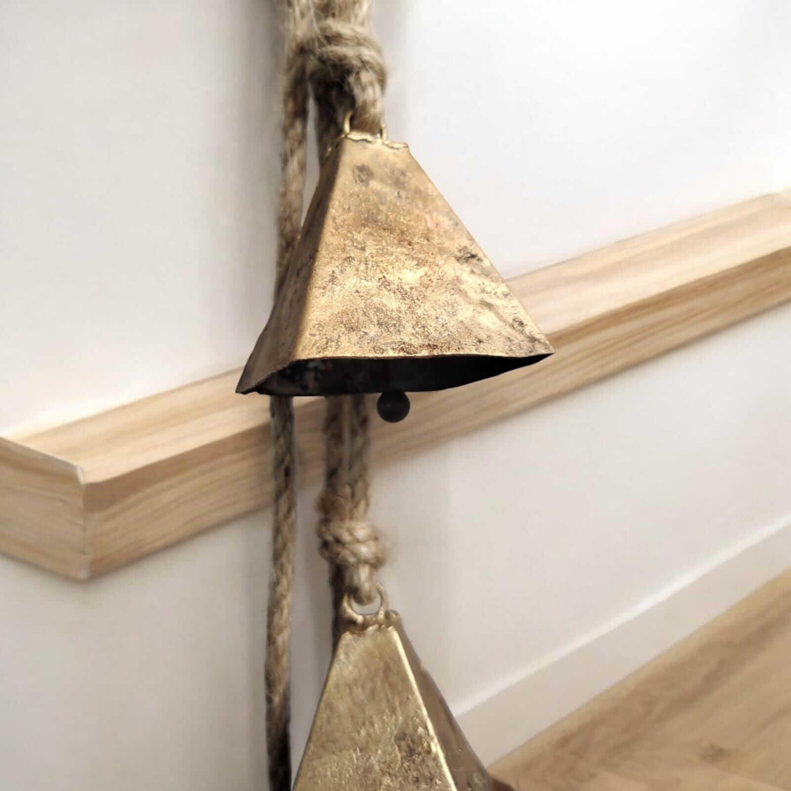 Rustic iron wind chime featuring antique cow bells hanging by jute rope for outdoor decor and soothing sounds.