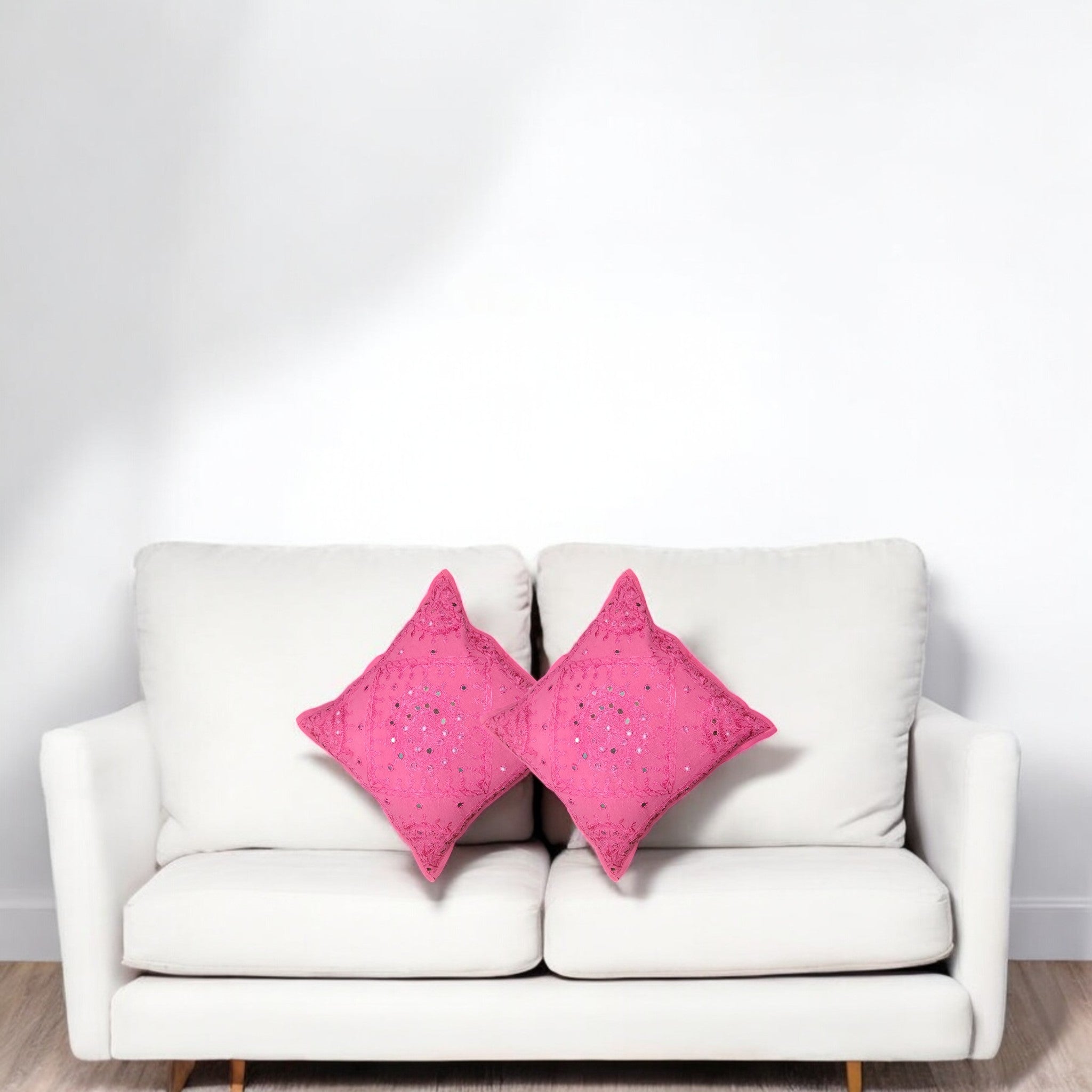 Set of 2 pink mirror work cushion covers on a sofa, enhancing home decor with handcrafted elegance.