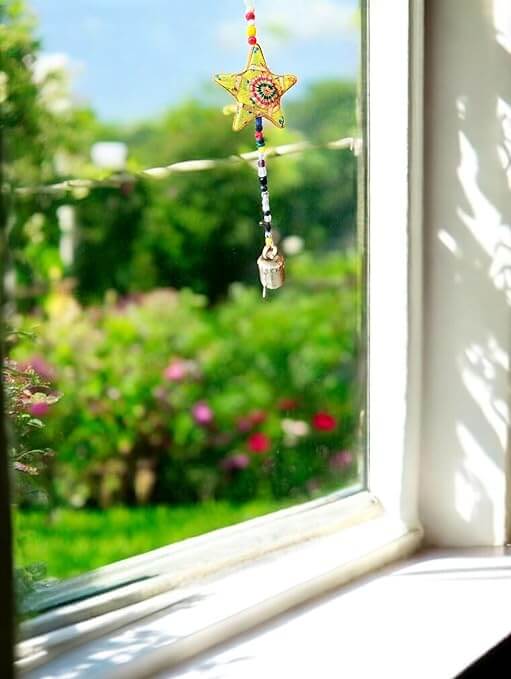 Handmade Star and Moon Door Hanging Mobile hanging in a window, featuring a decorative star and bright garden backdrop.
