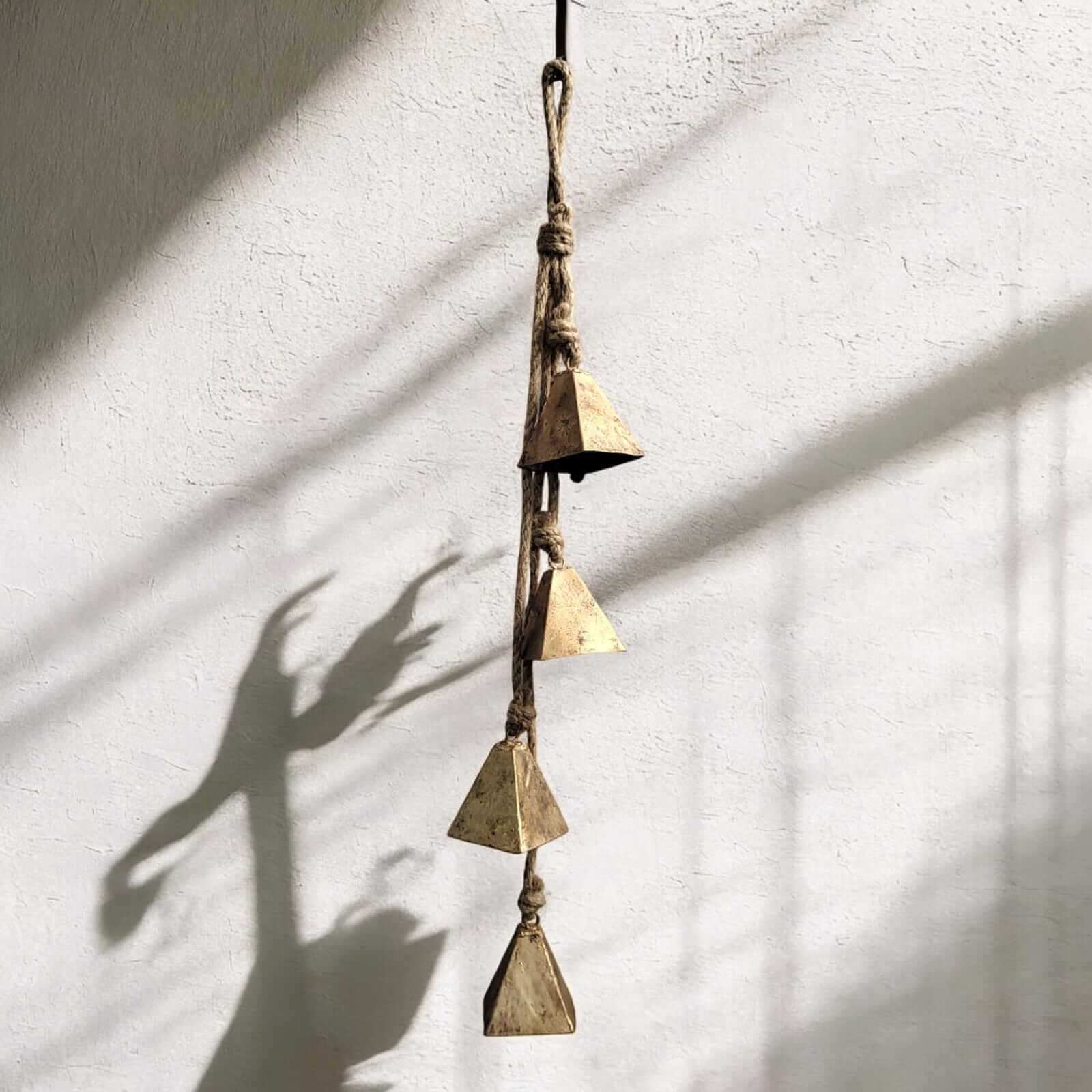Rustic iron wind chime with four vintage triangular bells hanging on jute rope, perfect for outdoor relaxation.