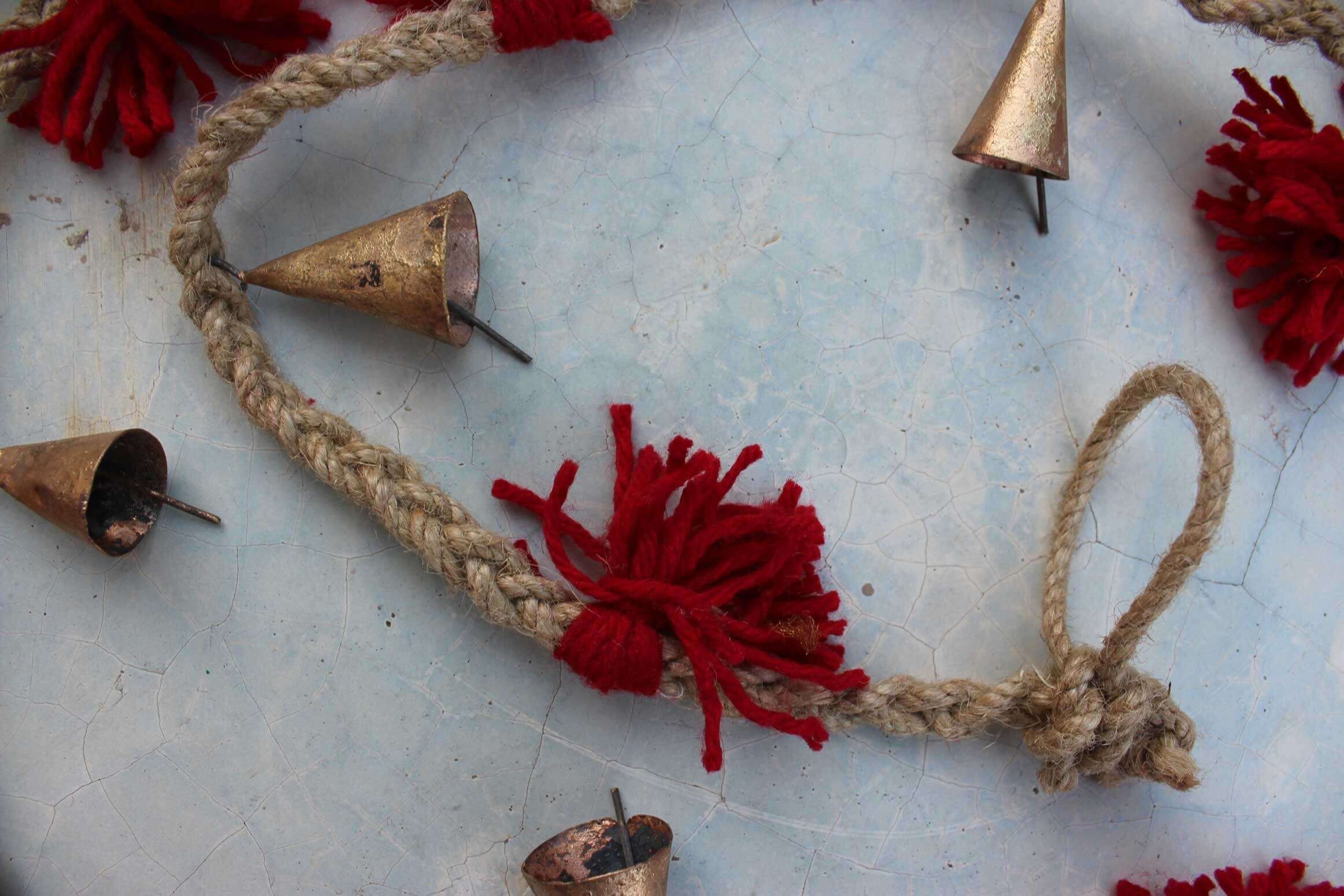 Vintage cow bells garland on jute string with red tassels, perfect for outdoor or garden decoration.