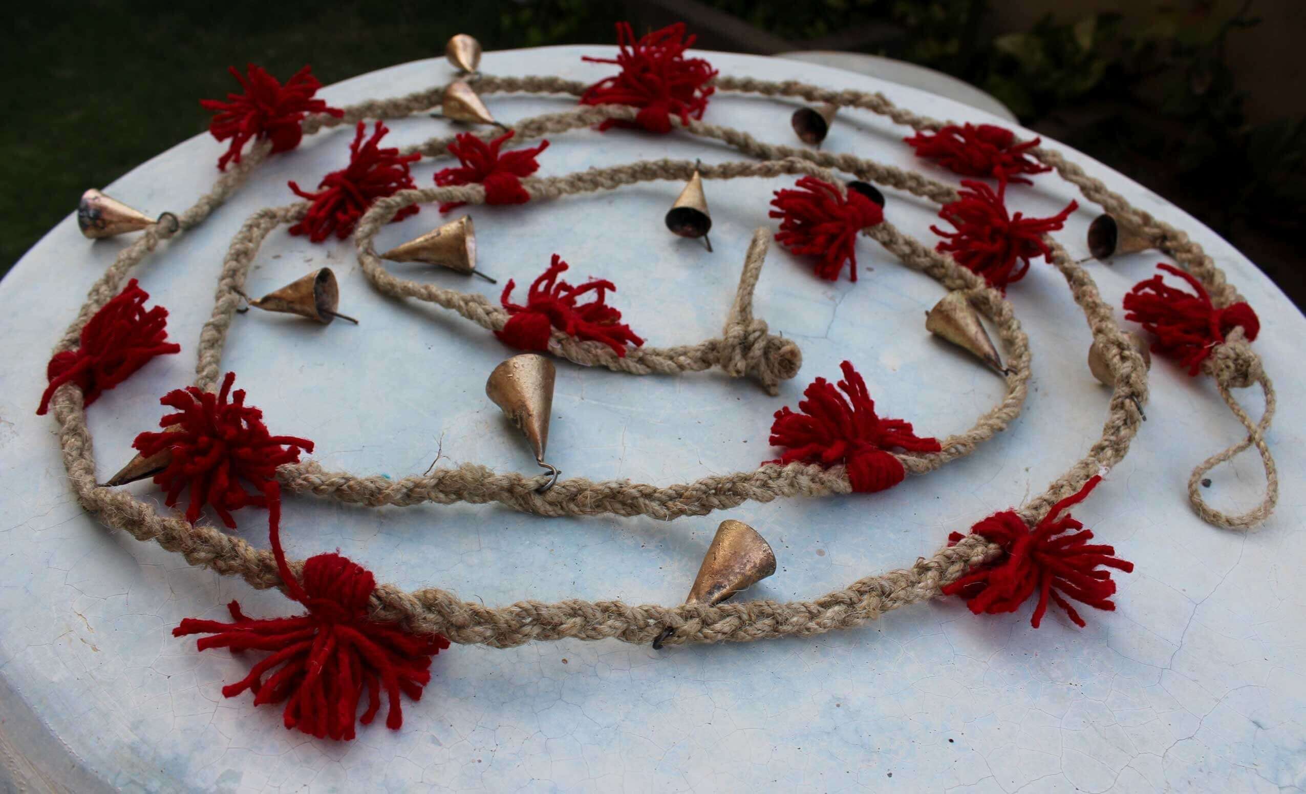Vintage cow bells garland on jute string with red wool tassels, perfect for garden and outdoor decoration.