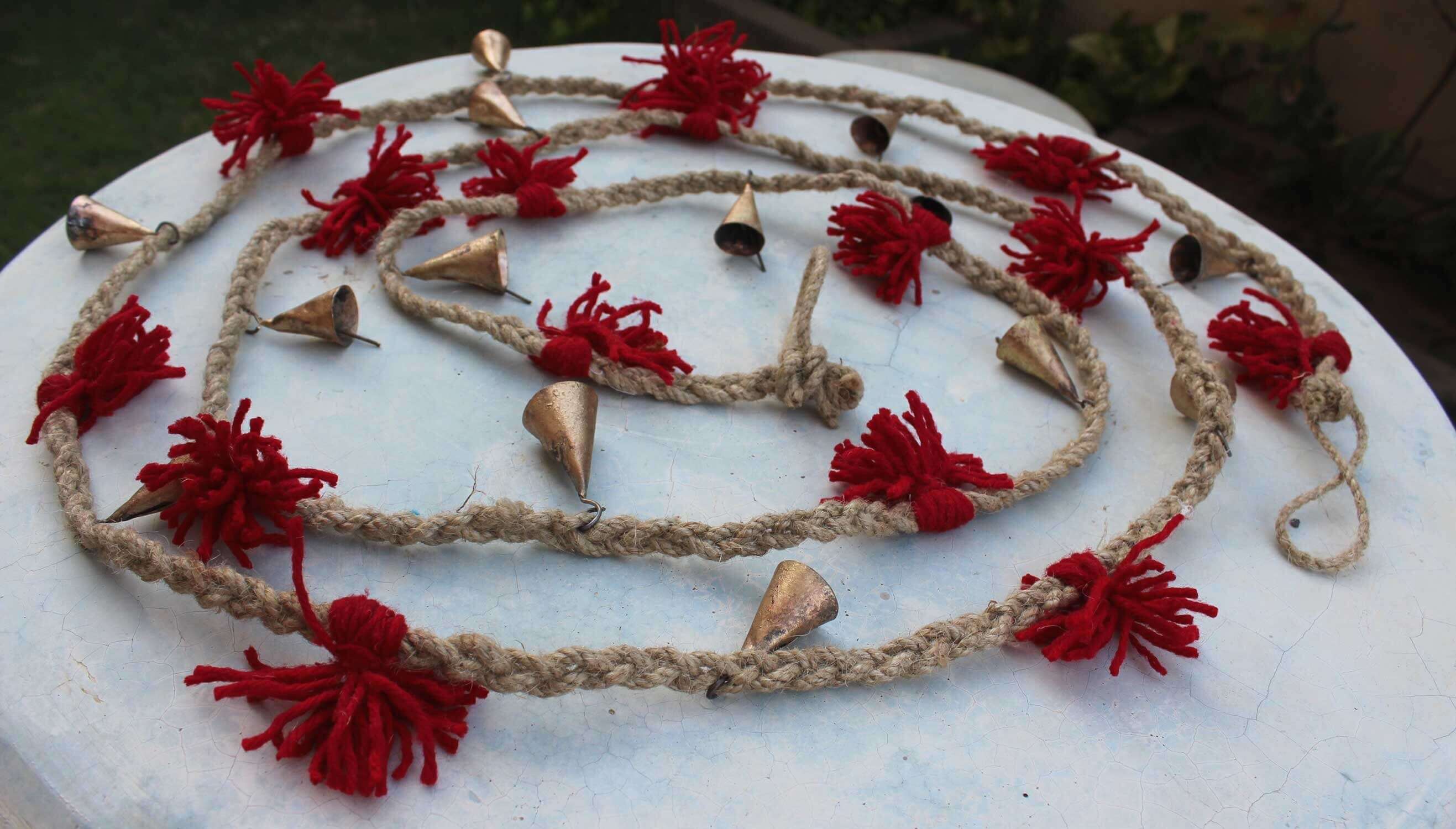 Vintage cow bells garland on jute with red wool tassels, perfect for outdoor and indoor decoration.
