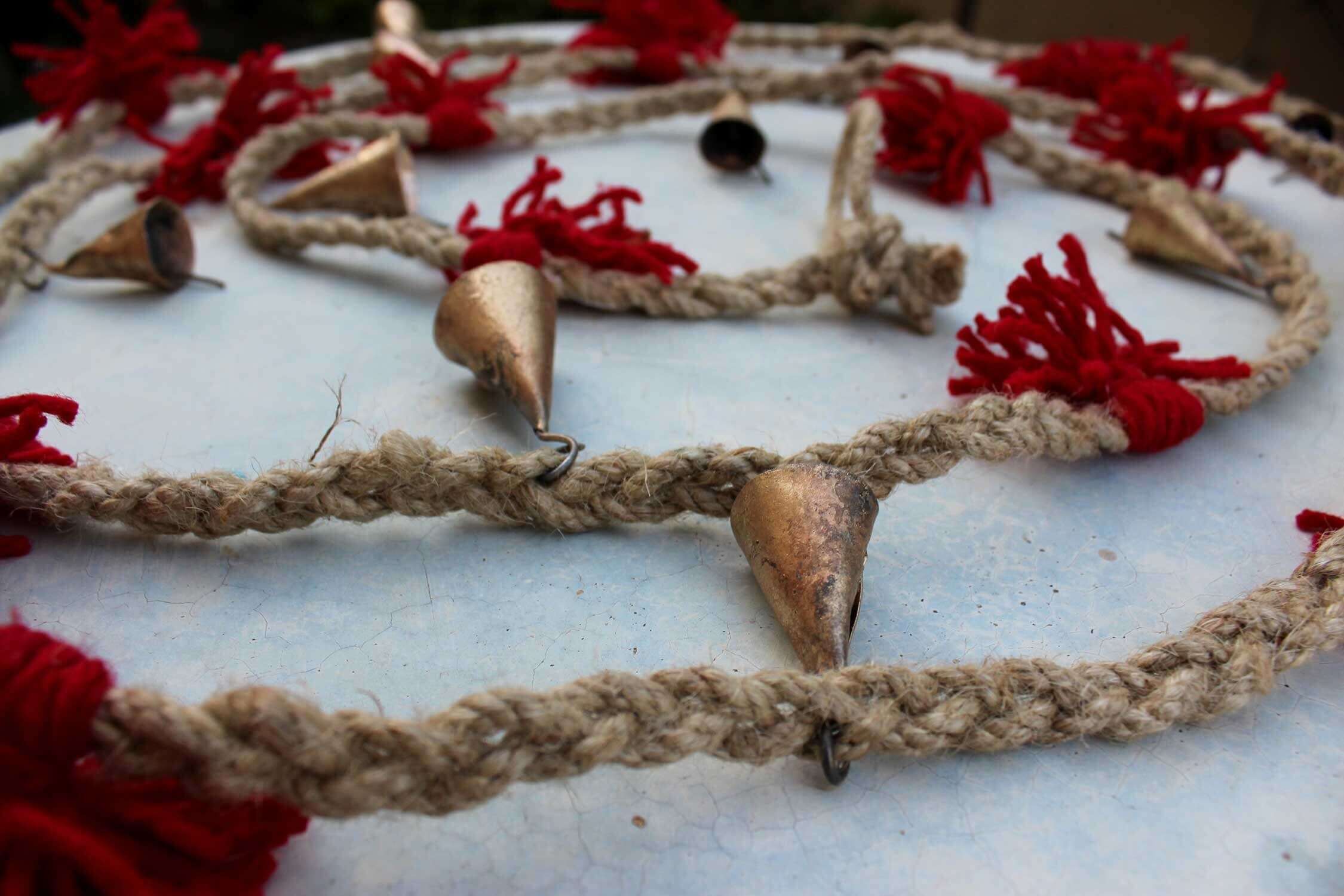 Vintage cow bells on jute string garland with red tassels, perfect for outdoor or indoor rustic decor.