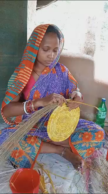 Woman weaving a bamboo wall plate with sabai grass in vibrant traditional attire, showcasing artisanal craftsmanship.