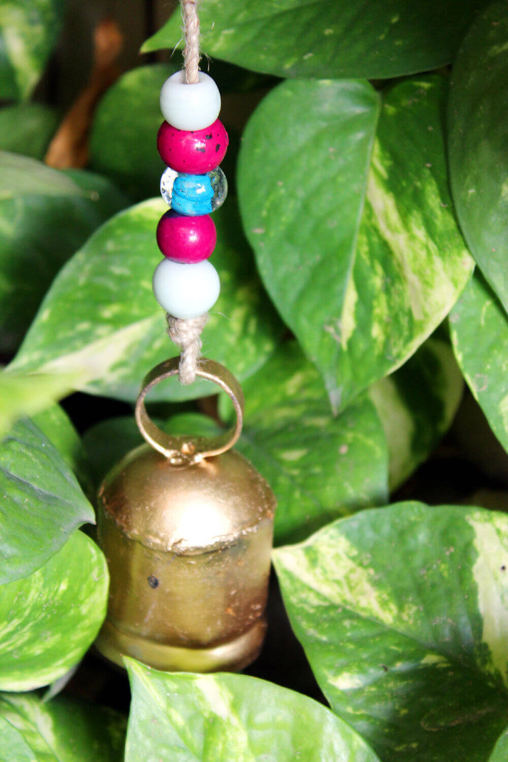 Hanging antique bell with colorful beads amidst lush green leaves, perfect for garden decor and relaxation.