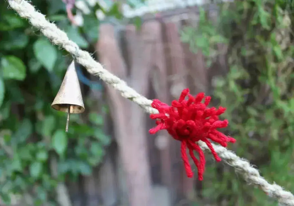 Vintage cow bell and red wool tassel on jute rope, perfect for rustic garden decor and outdoor hanging mobile.