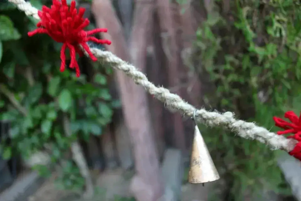 Vintage cow bell on jute rope garland with red wool tassels, perfect for outdoor decoration or rustic crafts.