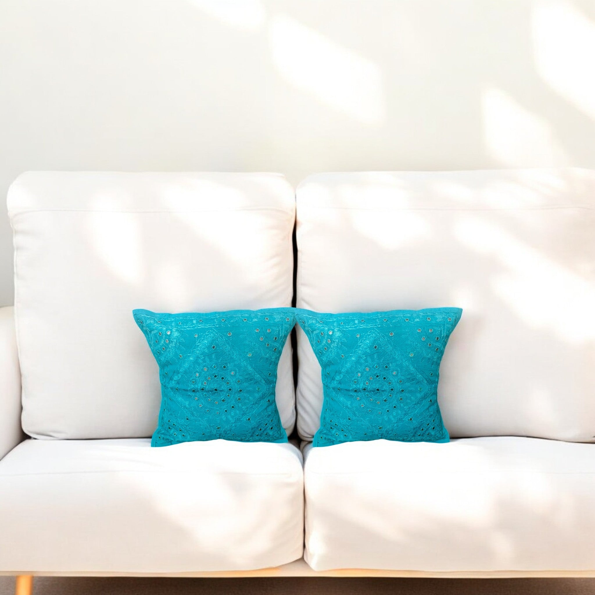Set of 2 turquoise blue handmade mirror work cushion covers on a white sofa, perfect for decorative accents.