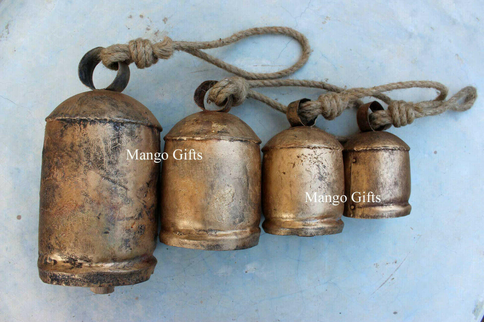 Set of 4 vintage handmade rustic iron cow bells on jute rope, perfect for garden décor and holiday decorations.