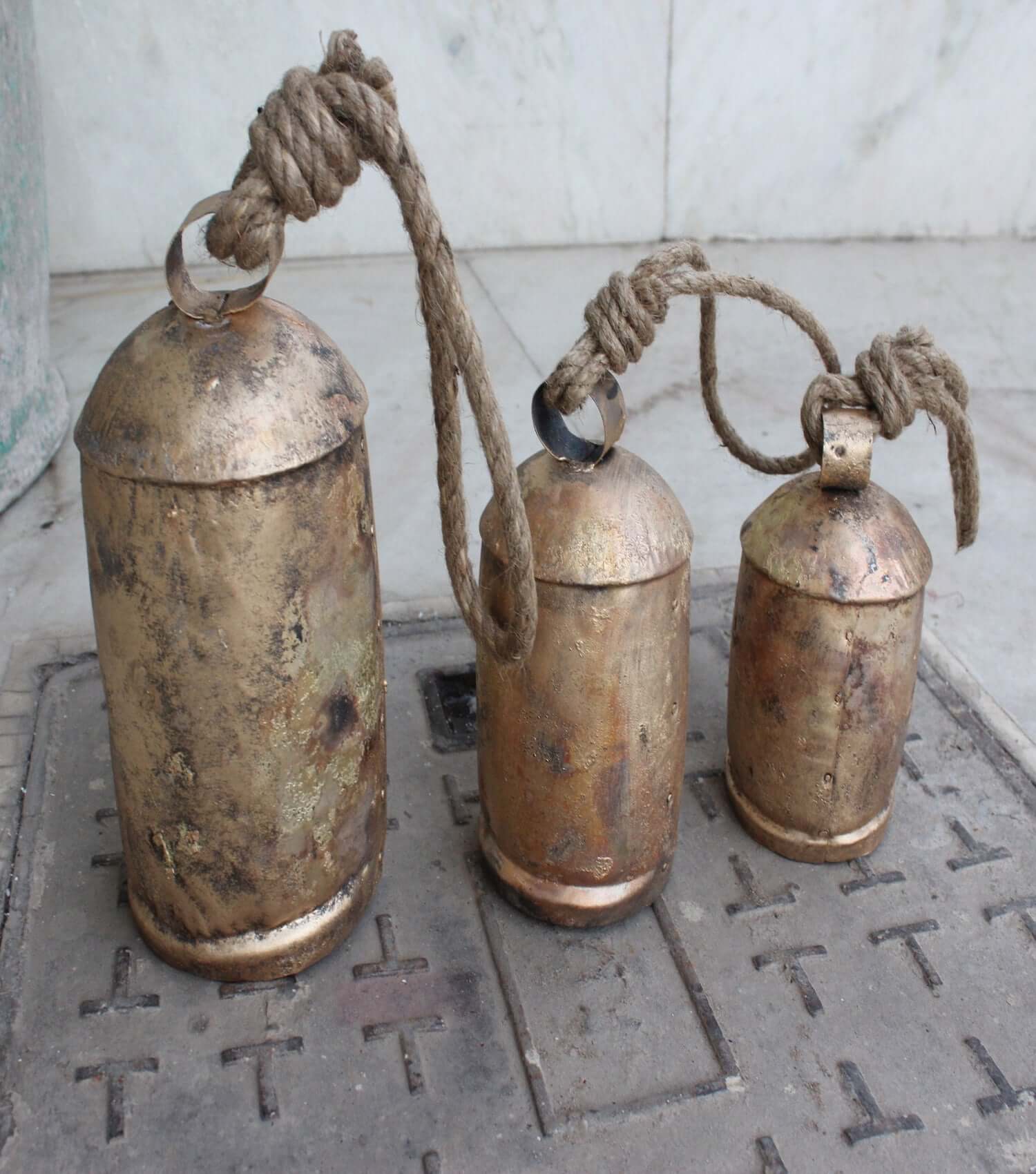 Set of 3 rustic iron cow bells with wooden clappers and rope hangers, antique finish, perfect for garden decor.