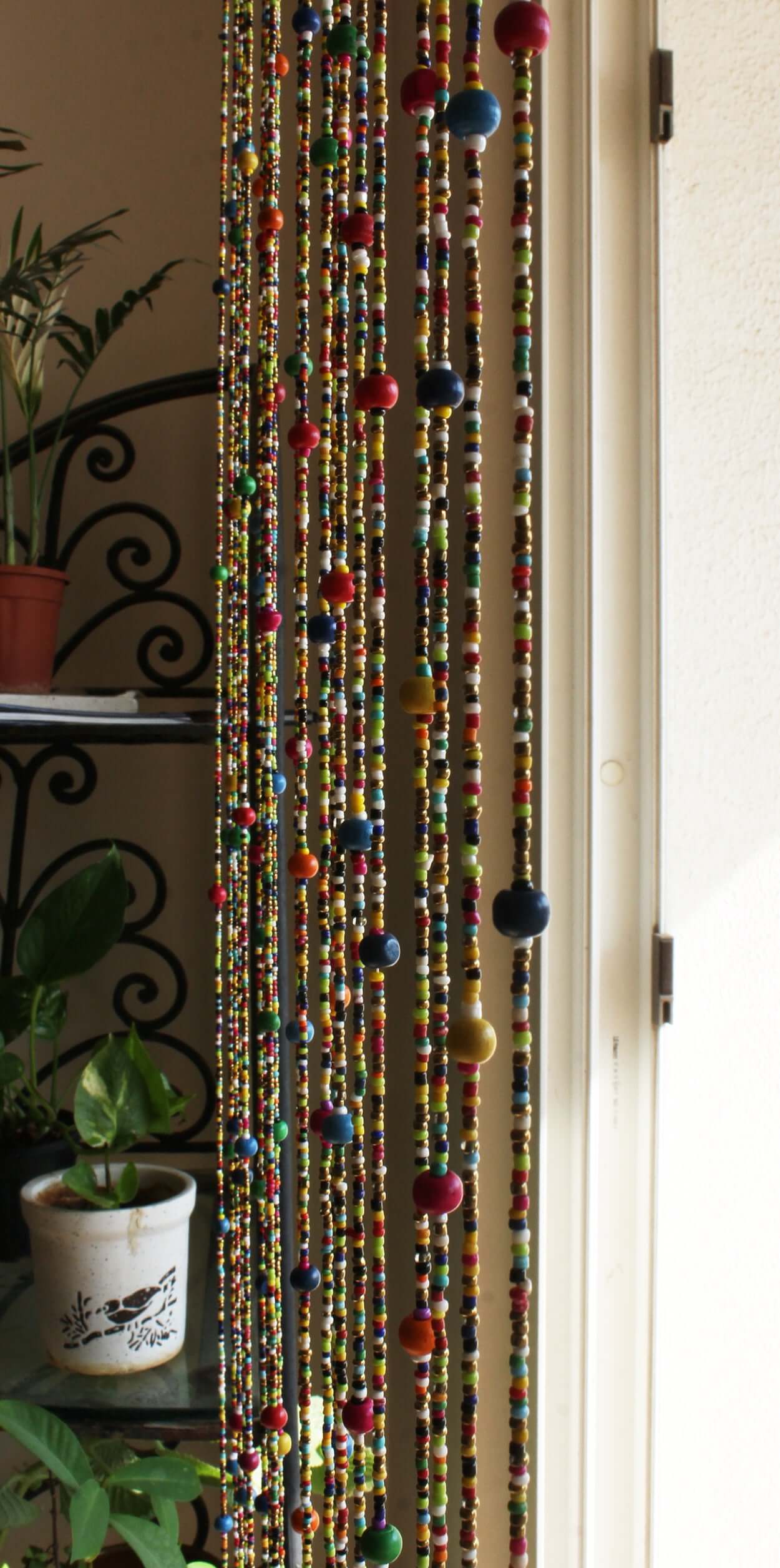 Colorful Bohemian beaded doorway garland with jingle bells hanging by a window, adding vibrant texture and charm.