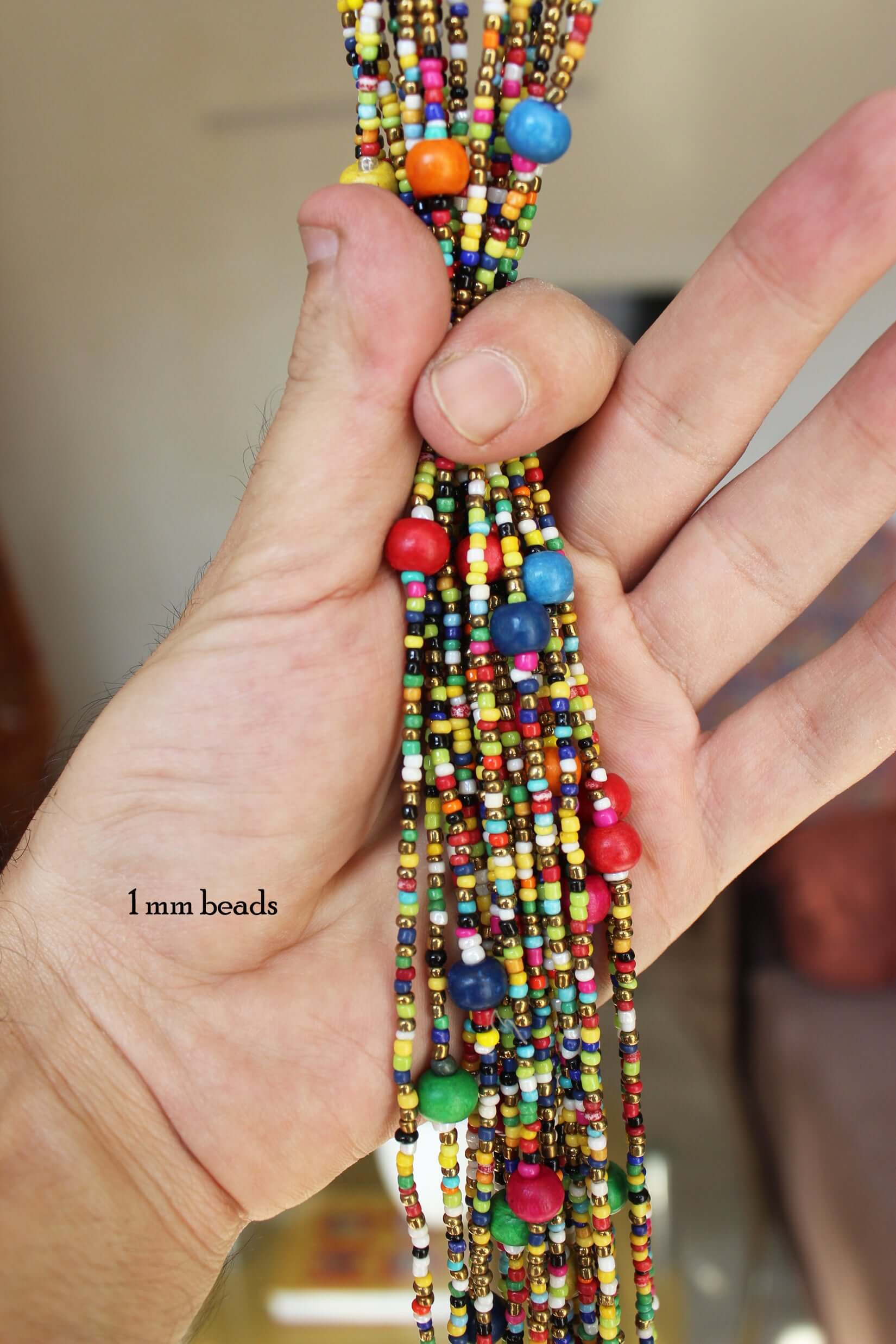 Hand holding colorful 1 mm glass beads for a bohemian doorway garland, showcasing vibrant patterns.