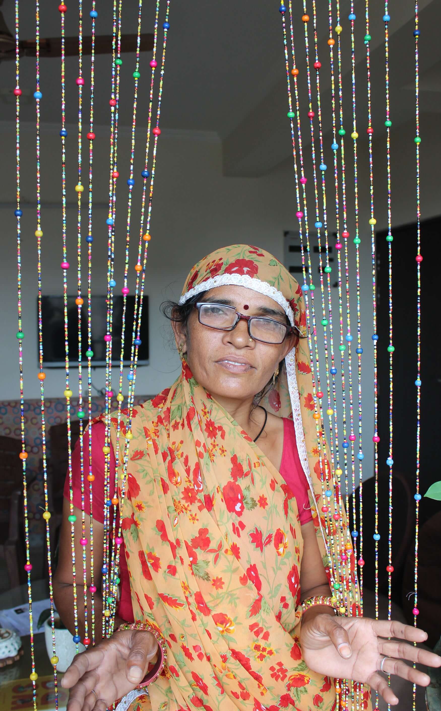 Woman in colorful attire behind a bohemian beaded doorway garland with jingle bells, showcasing vibrant decor.