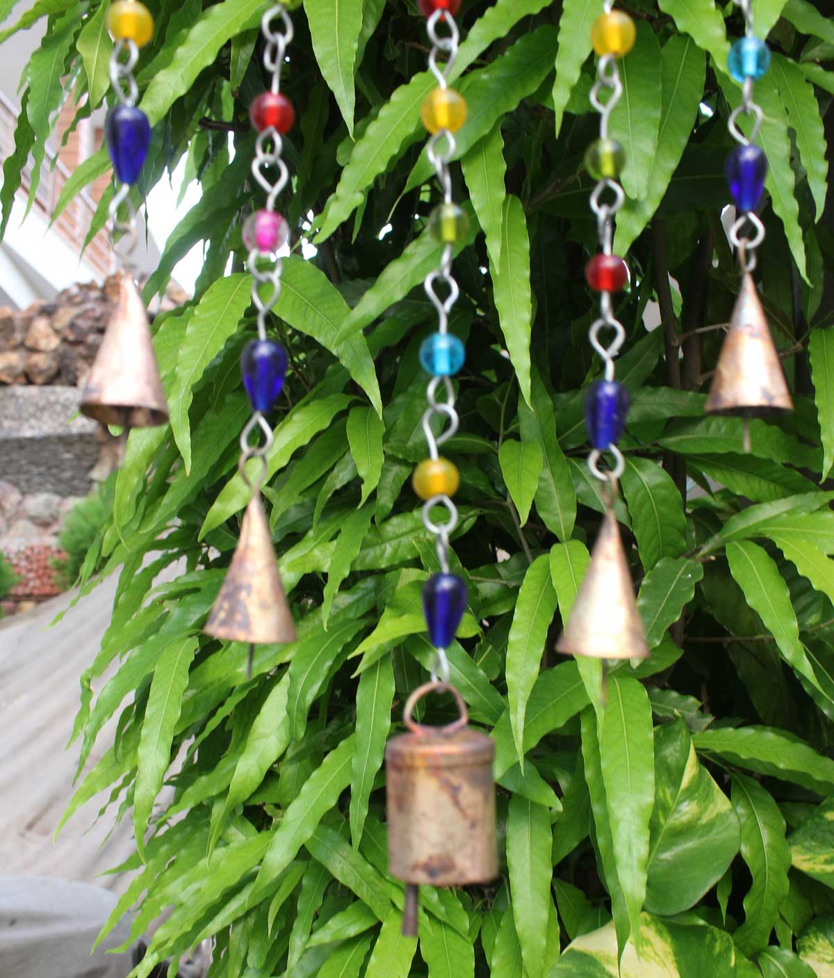 Handmade hanging chime bells and beads decoration, Bohemian design, green foliage background, indoor and outdoor use.