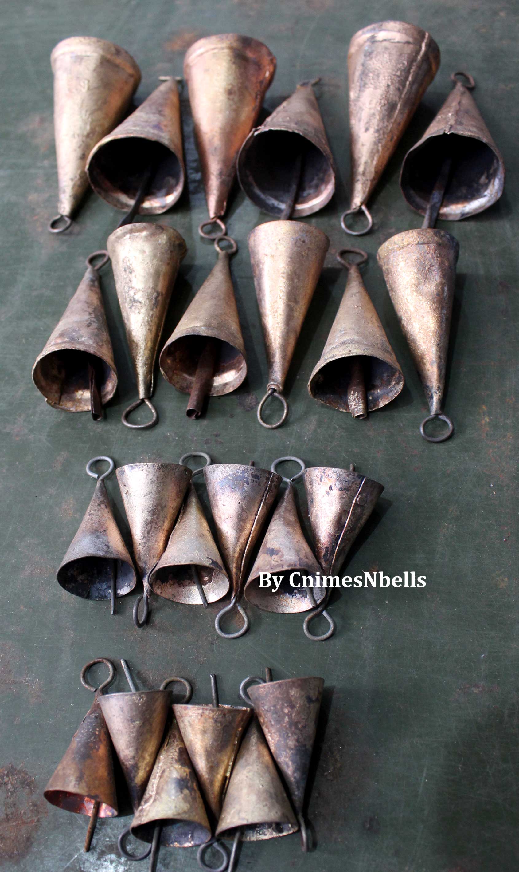 Set of 24 handmade recycled iron tin cowbells in various sizes, showcasing rustic brown tones and vintage charm.