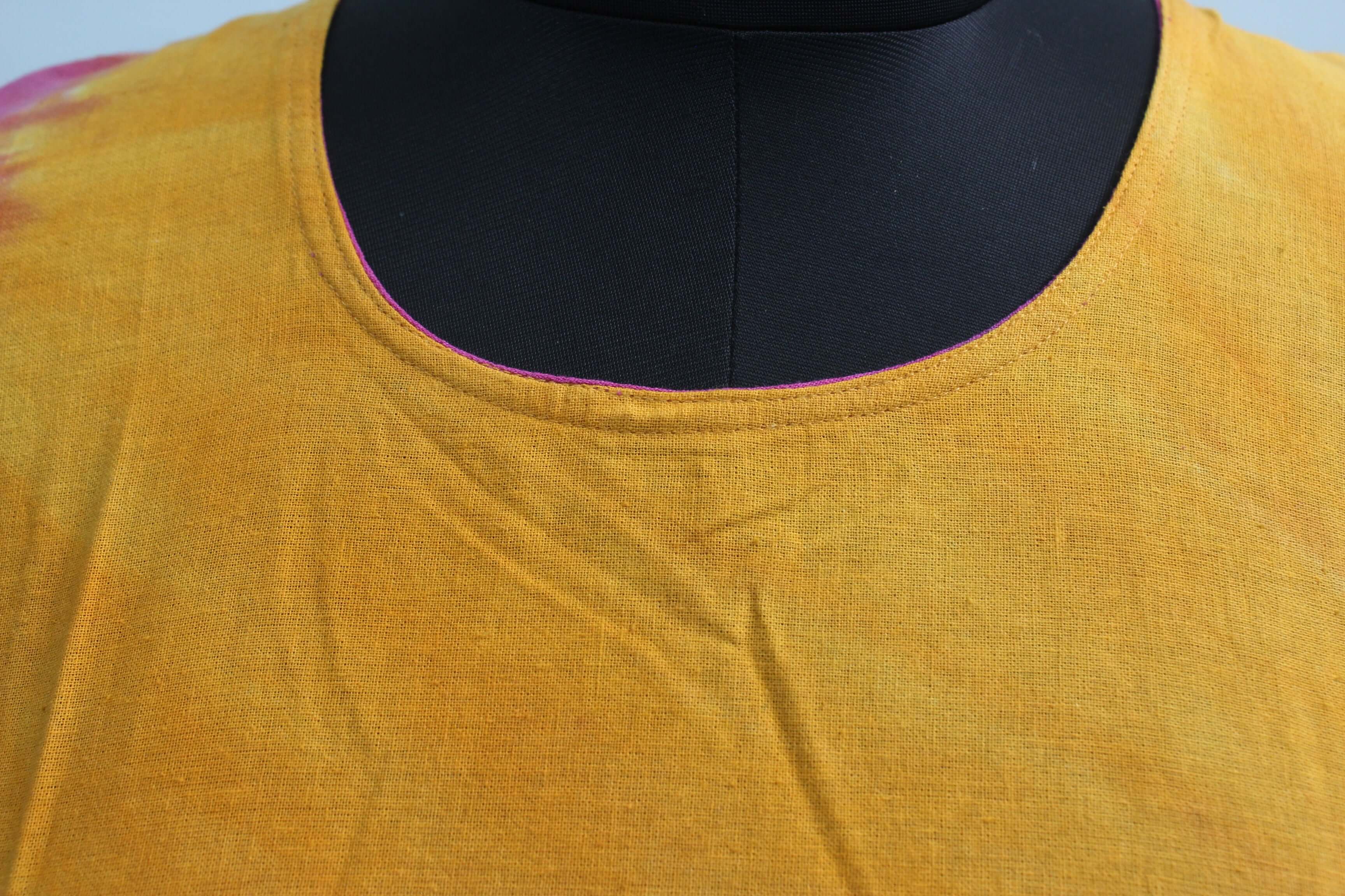 Close-up view of the neckline of a cotton tie-dye dress in vibrant yellow and pink colors.