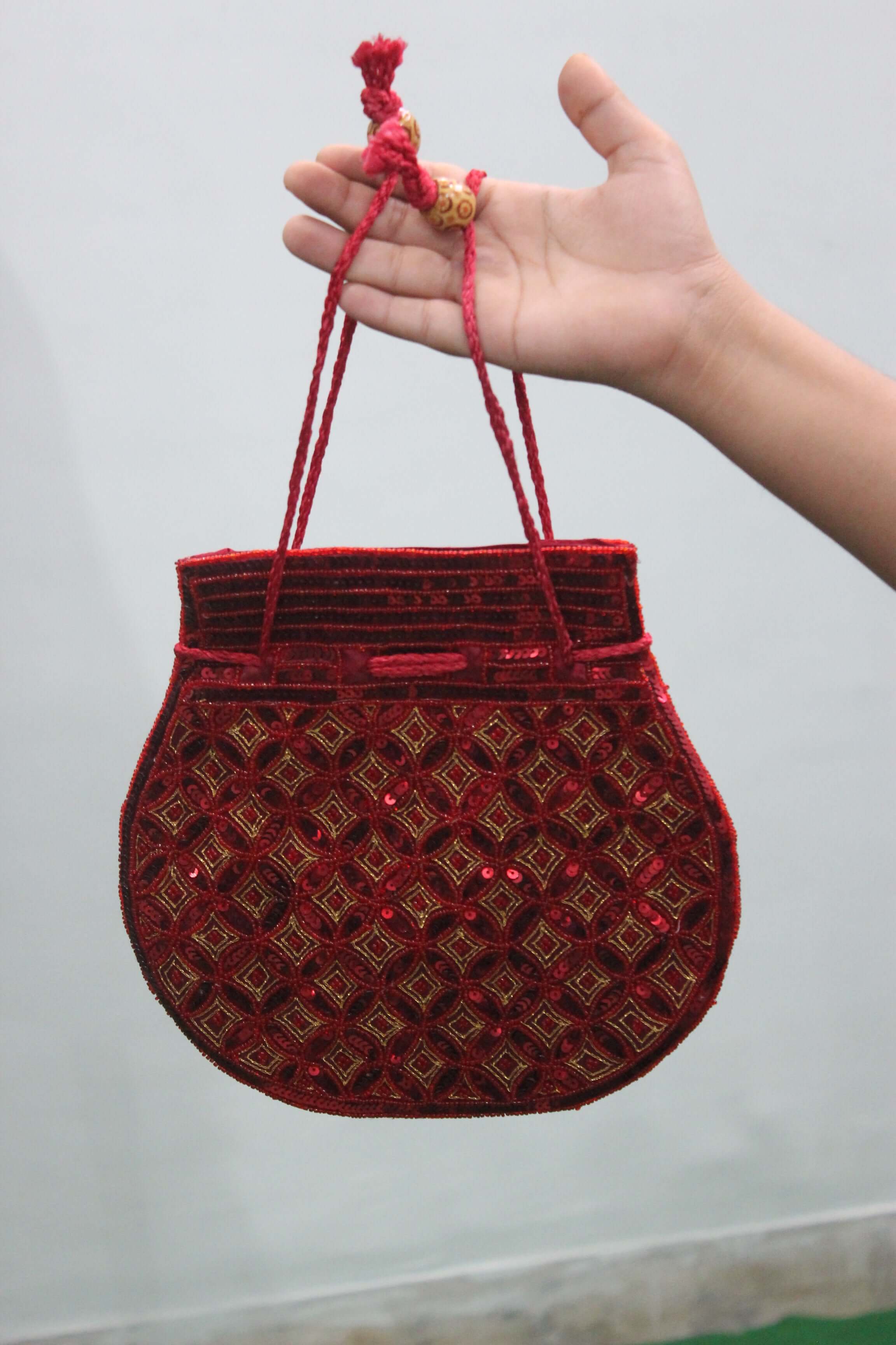 Beautiful red handmade Indian potli bag with sequins, ideal for carrying small articles, shown in hand.