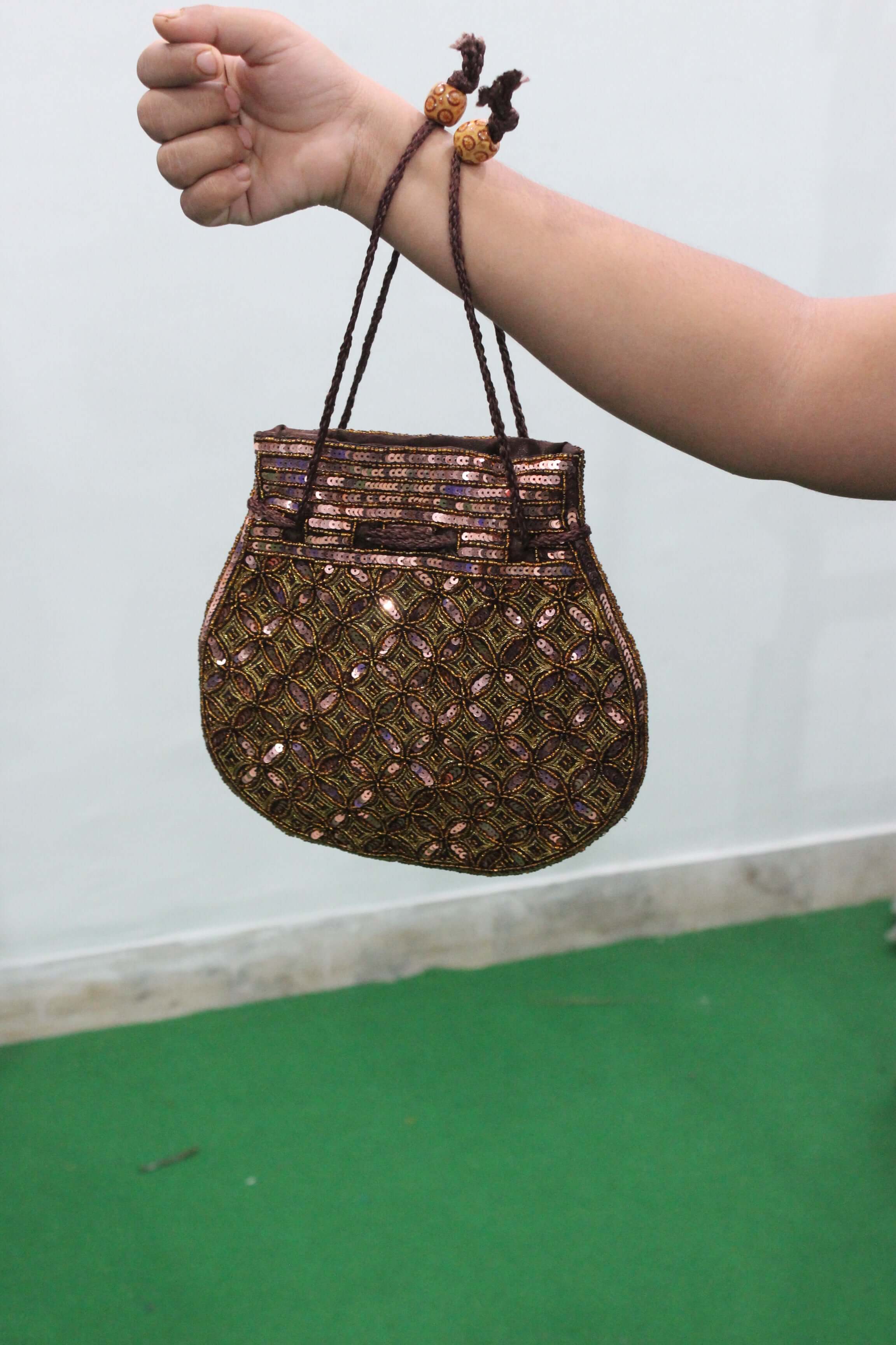 Brown golden sequin potli bag held in hand, featuring intricate design and drawstring closure.