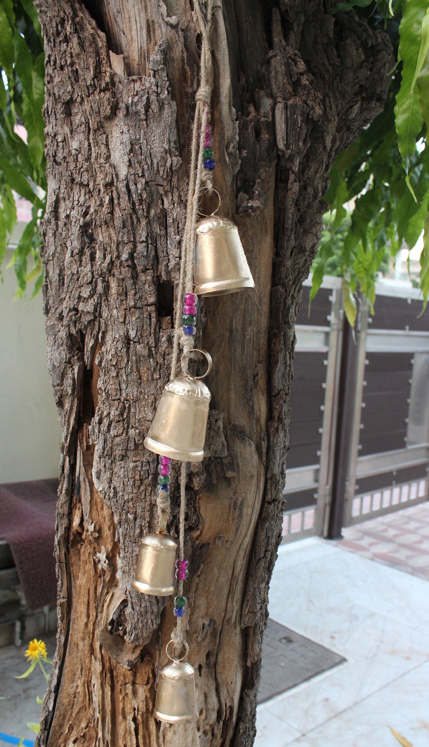 Handmade tin bells wind chime hanging on tree, adorned with glass beads for outdoor garden decoration.