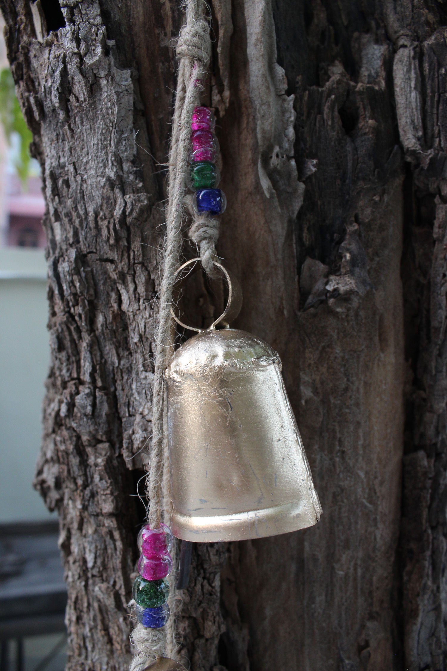 Handmade tin bell wind chime with glass beads, hanging on jute rope, suitable for outdoor patio and garden decoration.