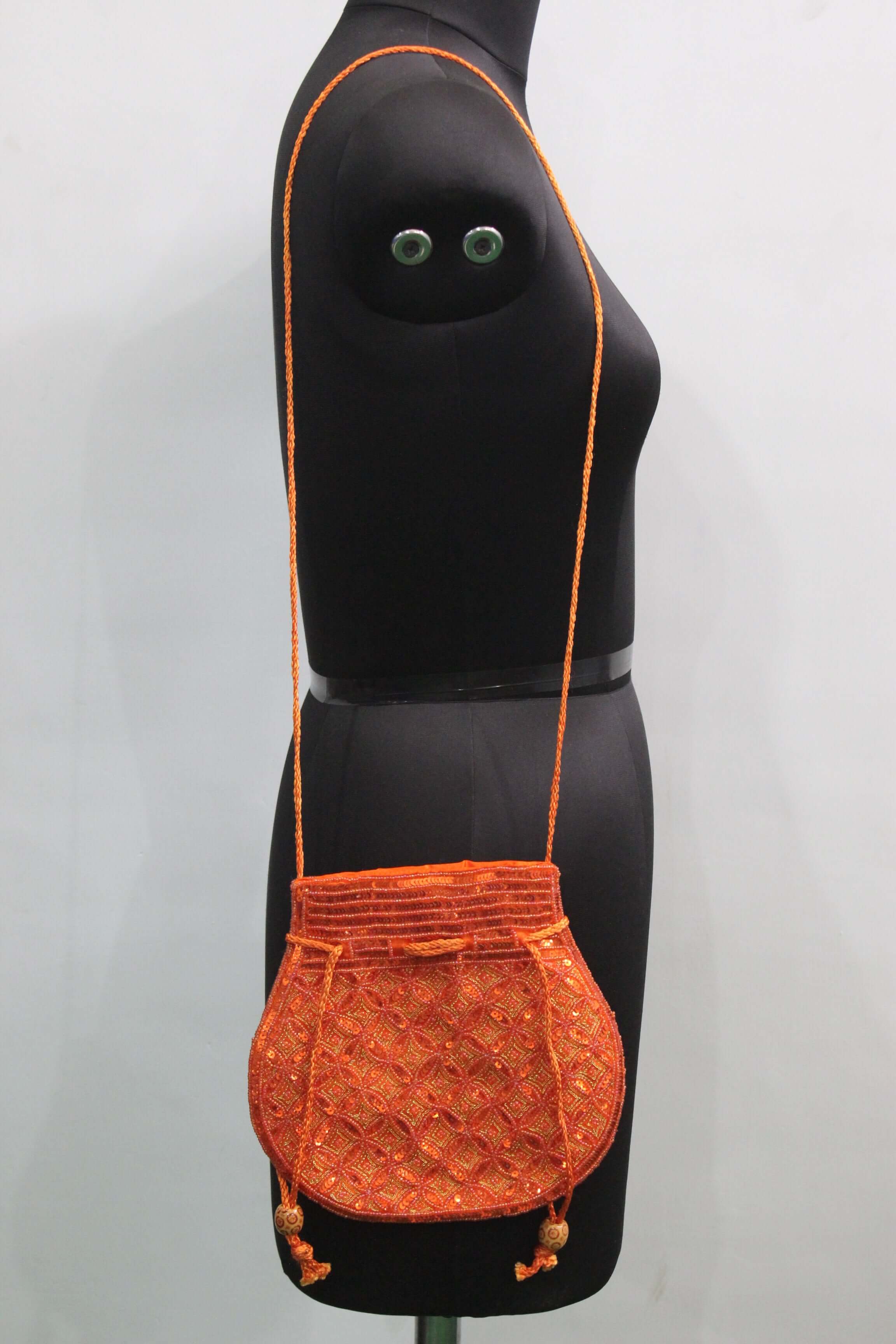 Beautiful orange handmade Indian potli bag with sequins, perfect for carrying small articles, shown on mannequin.