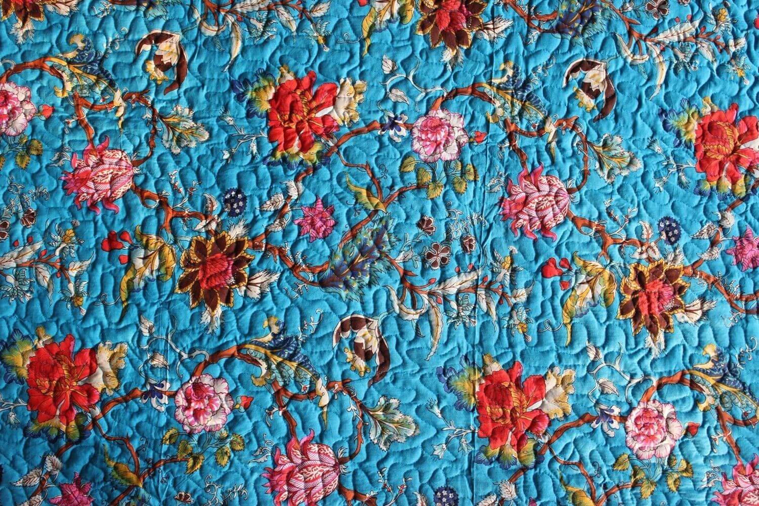 Blue floral reversible cotton quilt with vibrant red, pink, and green flowers pattern.