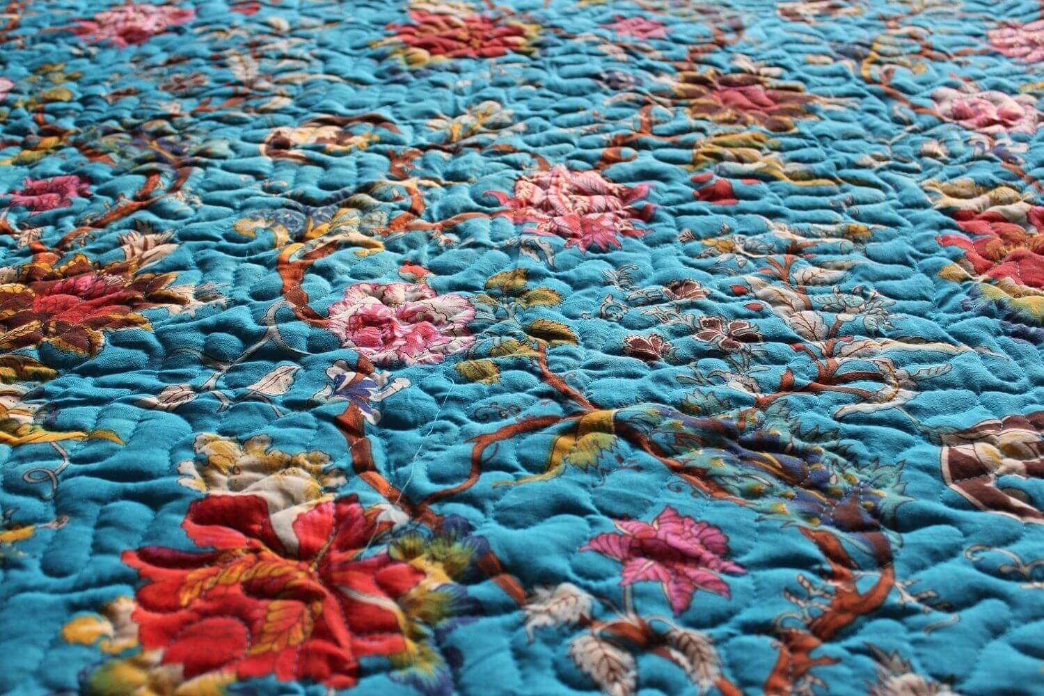 Close-up of a blue floral reversible cotton quilt with vibrant flower patterns and detailed stitching.